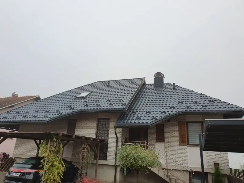 Temno siva kovinska kritina s strešnim oknom, snegobrani in žlebovi na zidani hiši