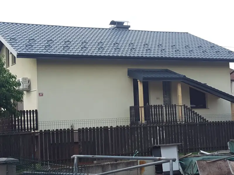 Temno siva kovinska kritina s snegobrani in nadstreškom nad vhodom na enonadstropni hiši