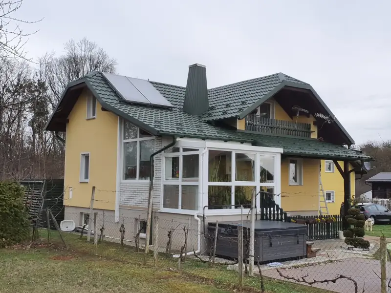 Zelena kovinska kritina z obrobljenim dimnikom in sončnimi kolektorji na družinski hiši